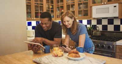 Husband showing his wife a funny news story on his tablet in their kitchen