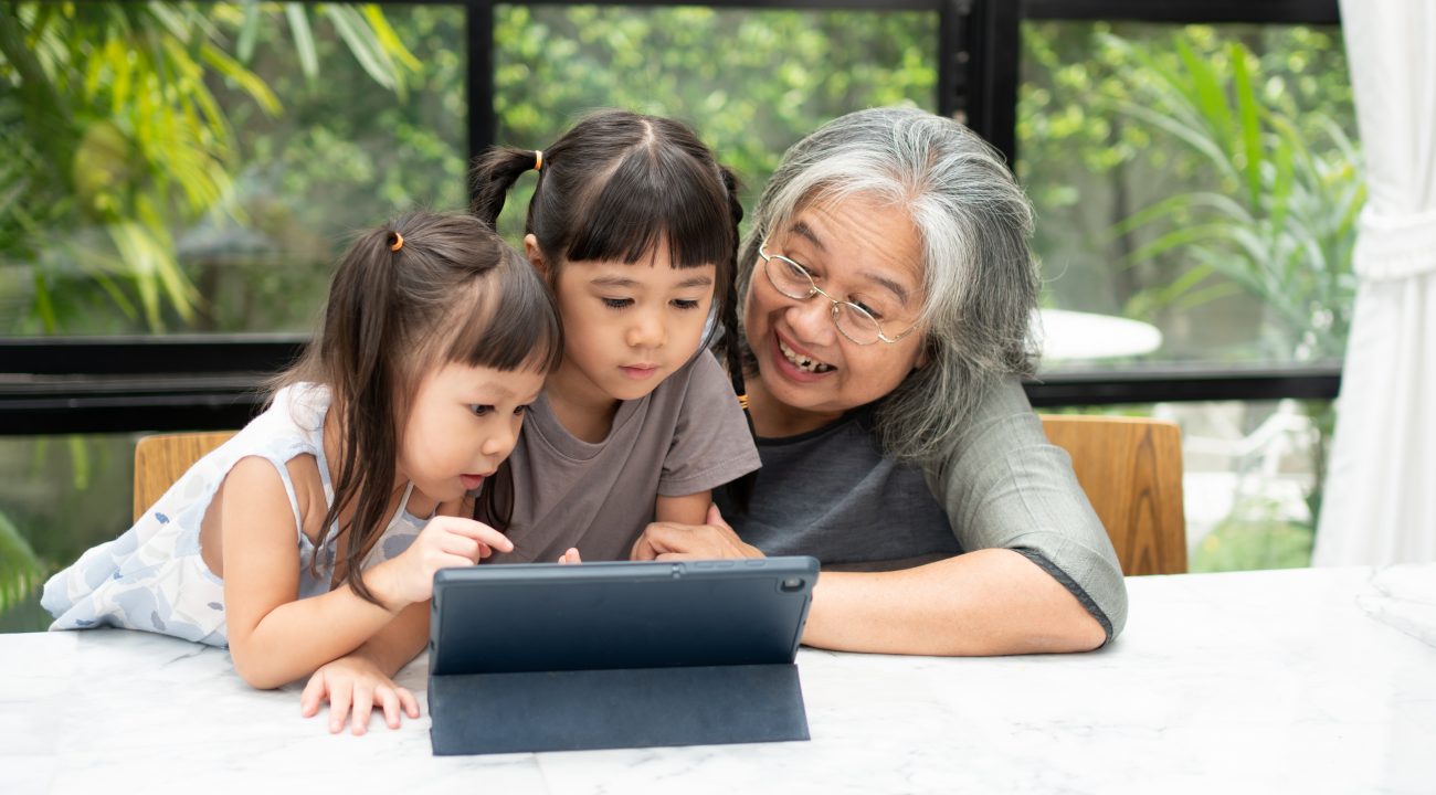 Asian Grandmother with her two grandchildren having fun and playing education games online with a digital tablet at home in the living room. Concept of online education and caring from parents.