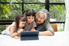 Asian Grandmother with her two grandchildren having fun and playing education games online with a digital tablet at home in the living room. Concept of online education and caring from parents.