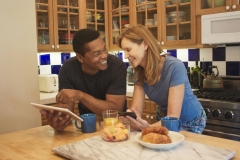 Husband showing his wife a funny news story on his tablet in their kitchen